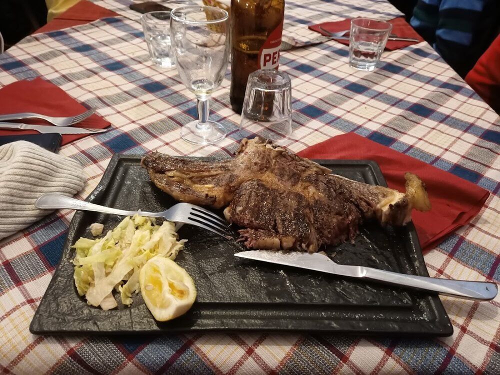 Una bistecca con l'osso appena tolta dalla griglia, servita su una pietra scura con insalata e mezzo limone.