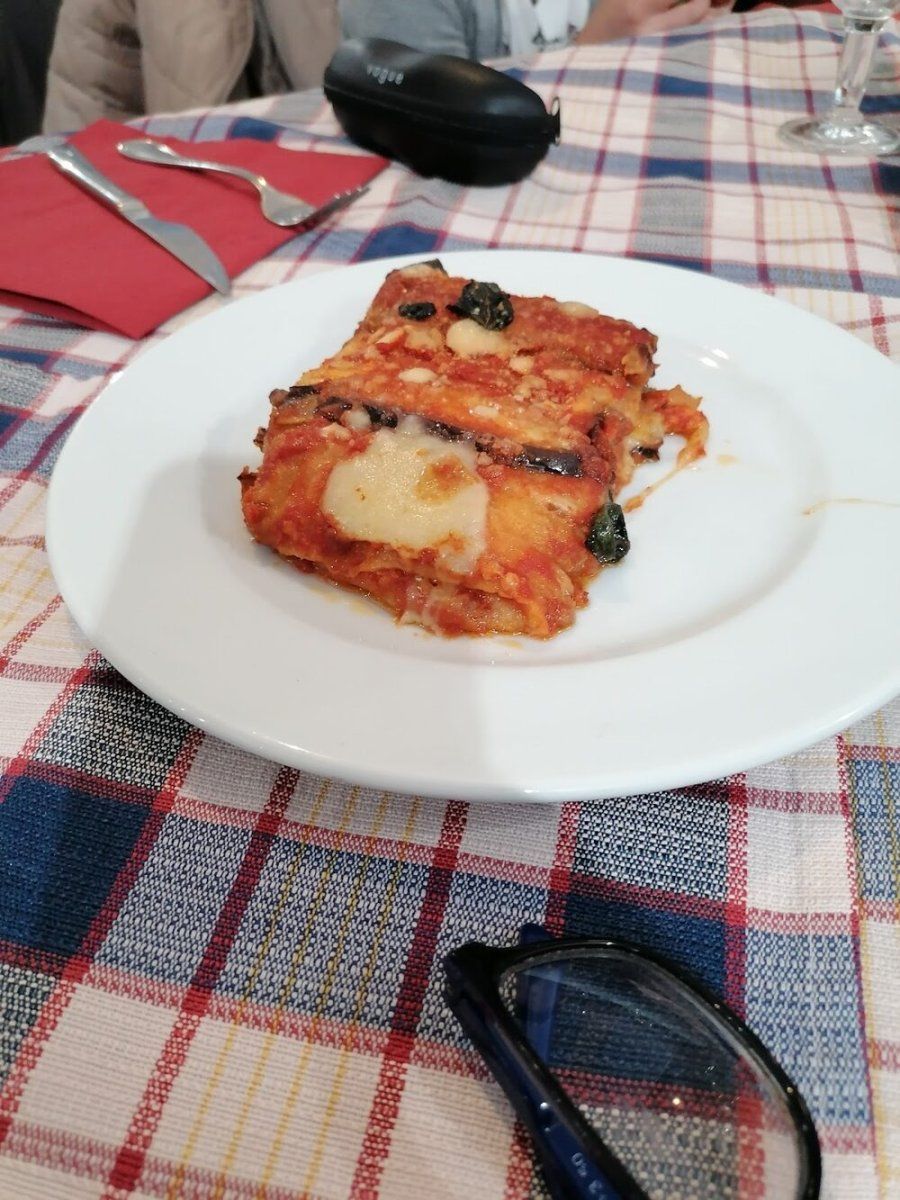Una porzione di parmigiana di melanzane con pomodoro, mozzarella filante e basilico, servita nel piatto bianco.